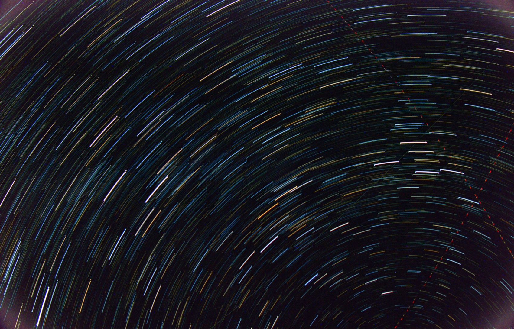 Star trails: hundreds of short parallel arcs of coloured light across a dense star field, all curving gently around the same distant point