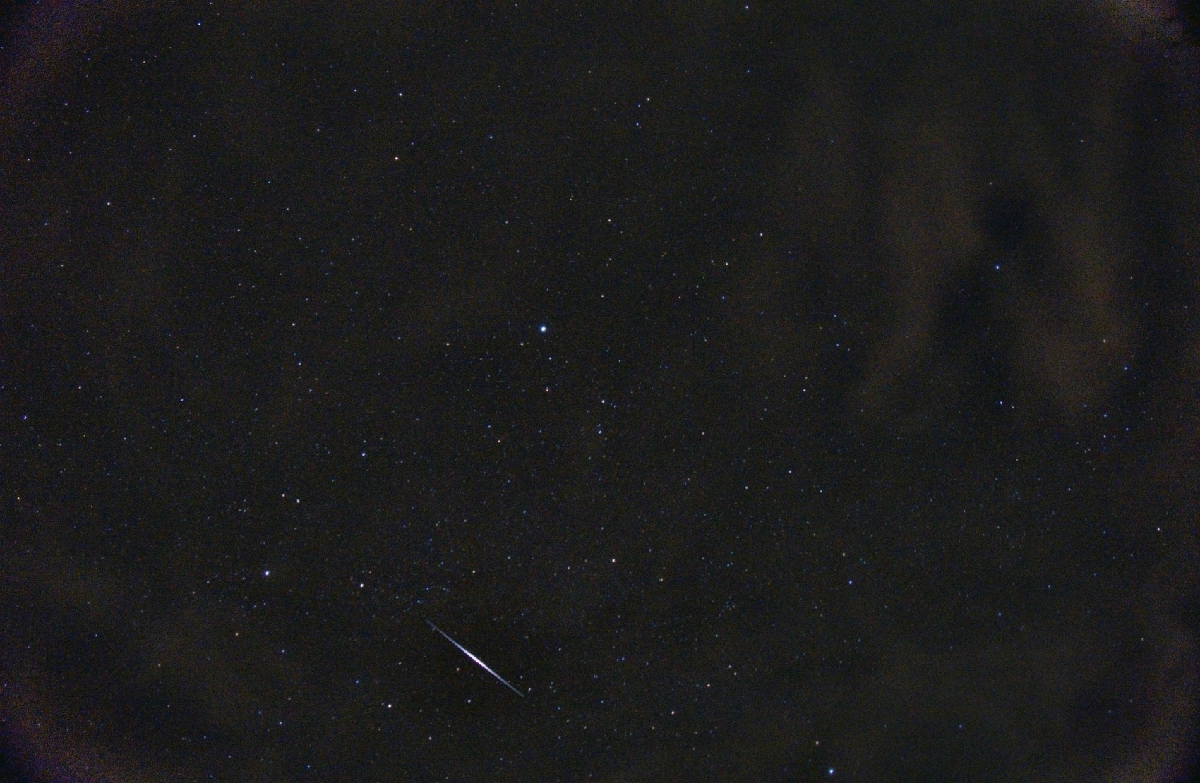 A single exposure of a star field with one brilliant tapered streak, bright in the middle and thinning at both ends, crossing the lower part of the frame