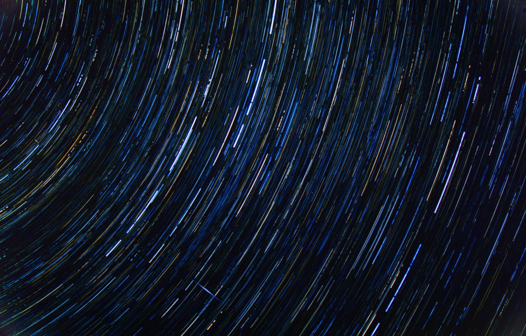 Long concentric star trails curving around a point beyond the top-left corner, the arcs broken into segments where cloud interrupted the sequence